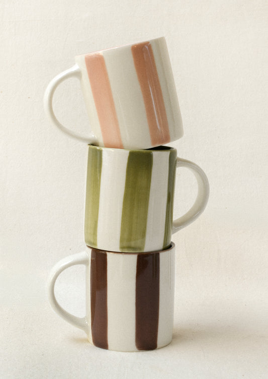 A stack of small ceramic espresso cups: one with pink stripes, one with green stripes, and one with brown stripes.