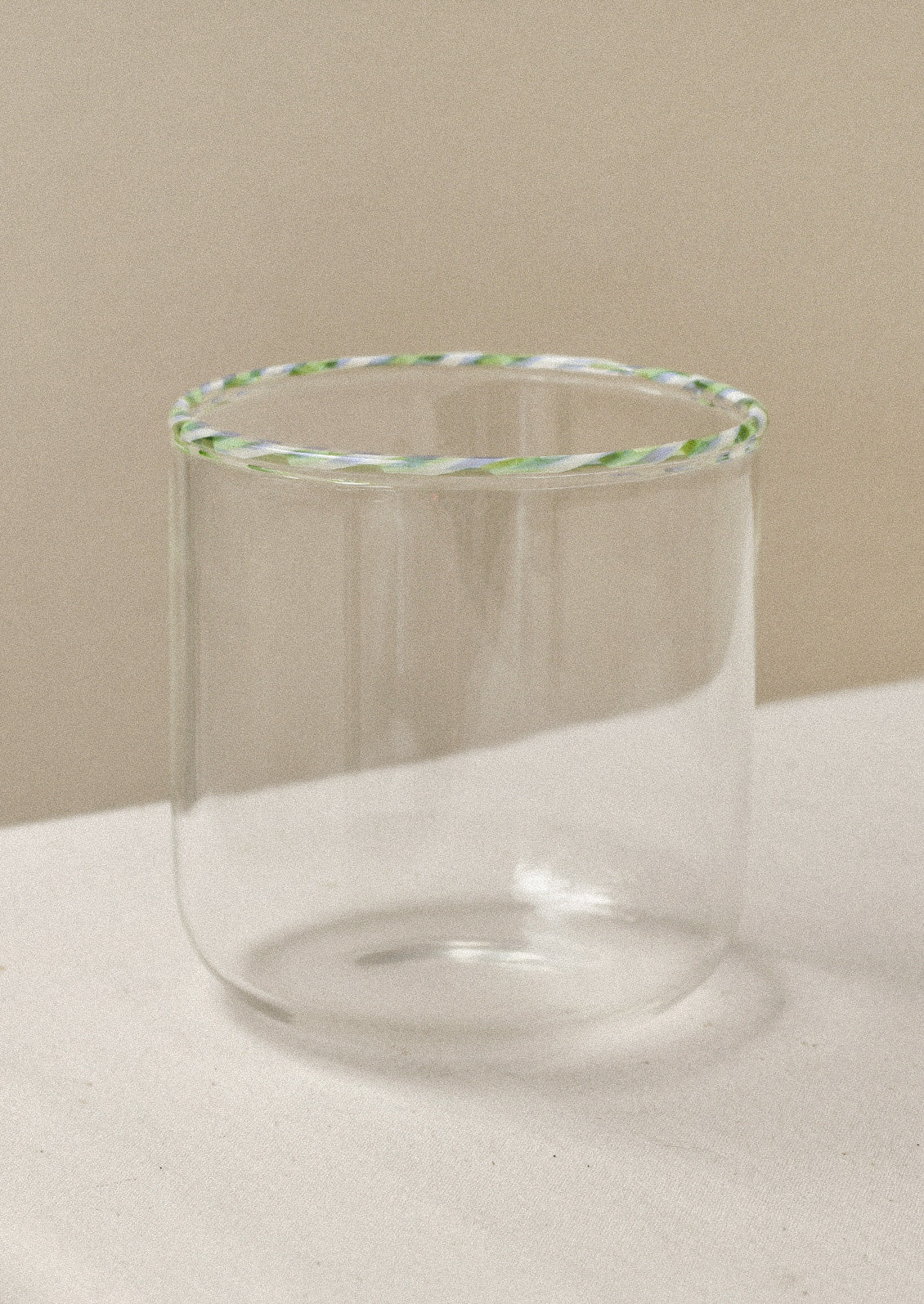 A clear drinking glass with a green striped rim