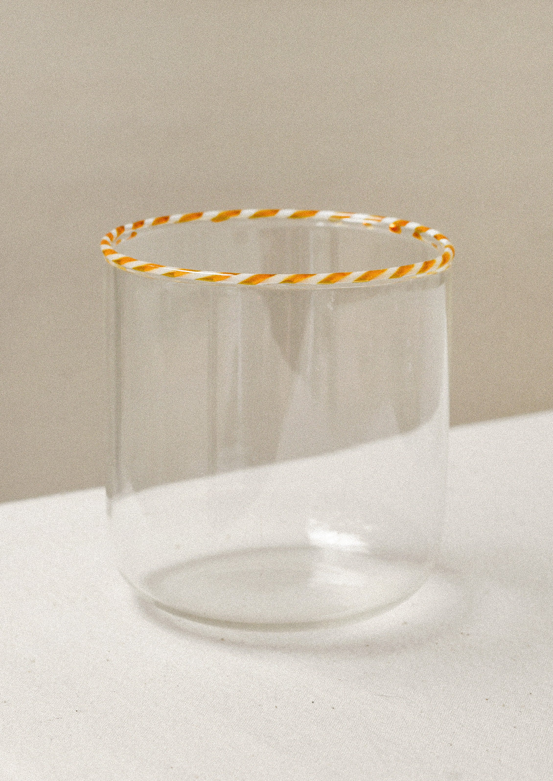 A clear drinking glass with an orange striped rim
