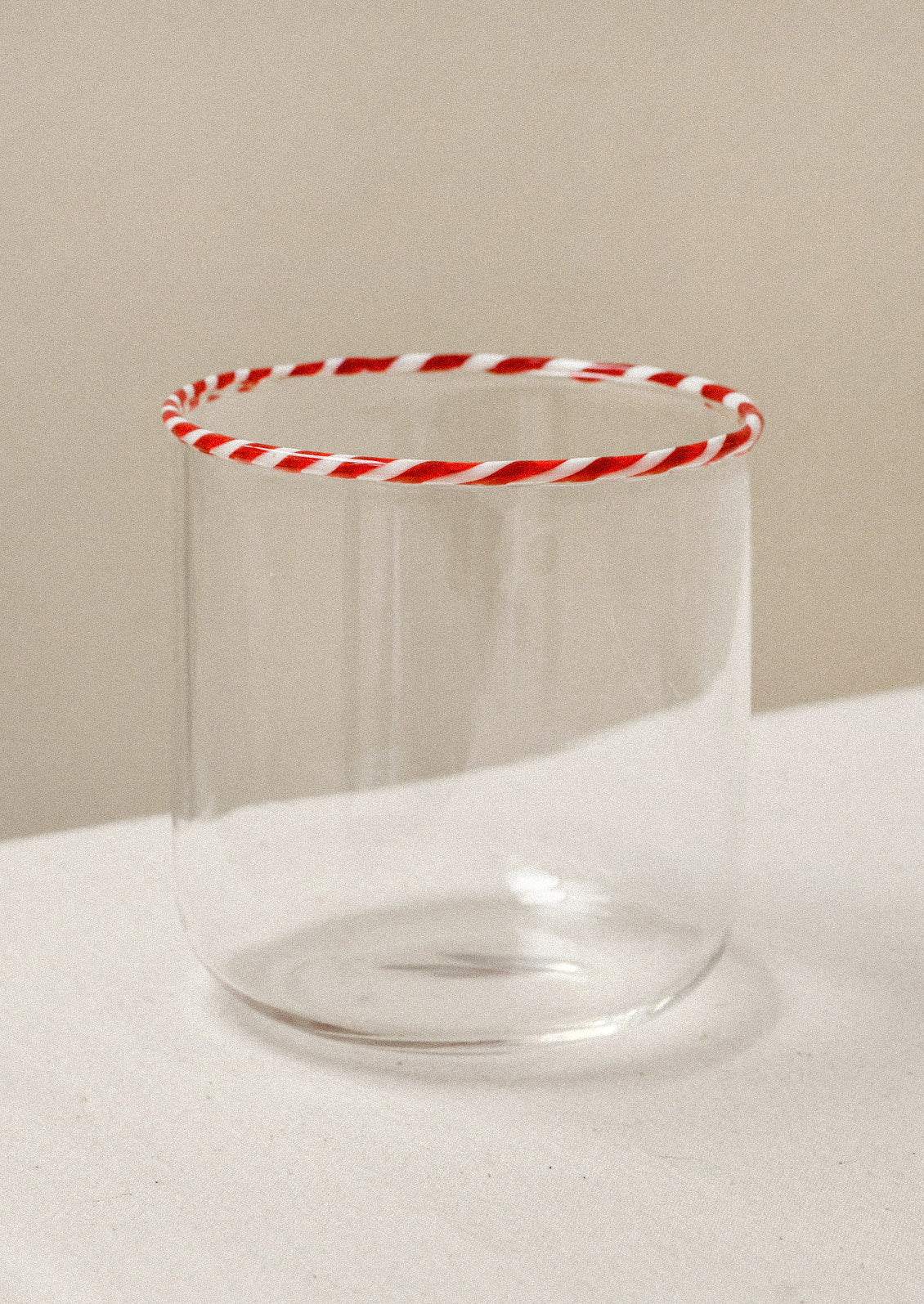 A clear drinking glass with a red striped rim