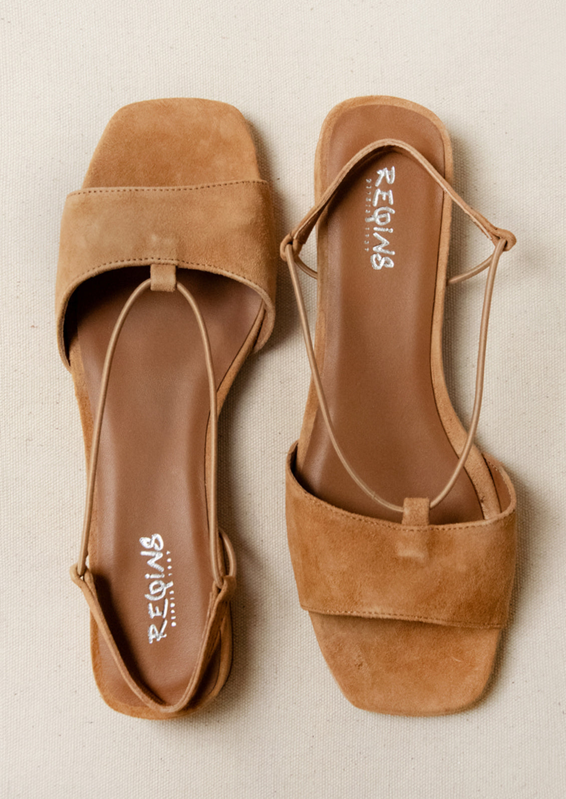 A pair of suede slingback heeled sandals in a camel color.