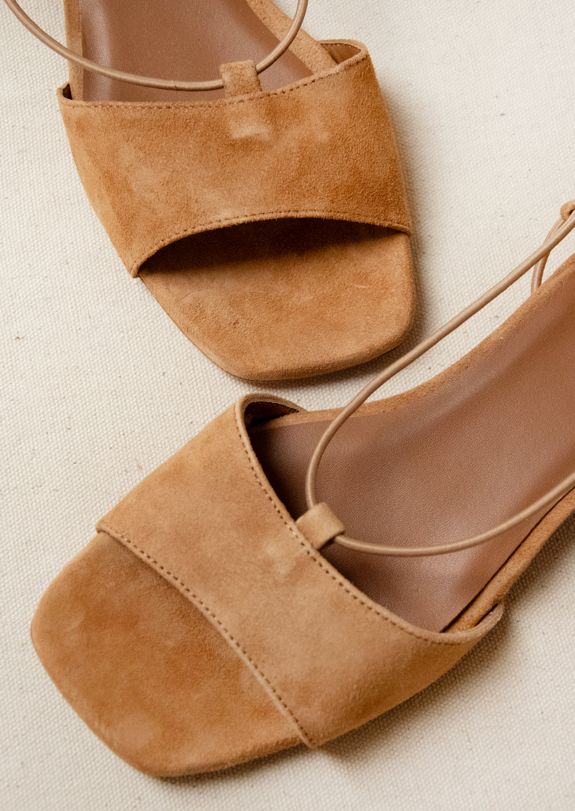 A pair of suede slingback heeled sandals in a camel color.