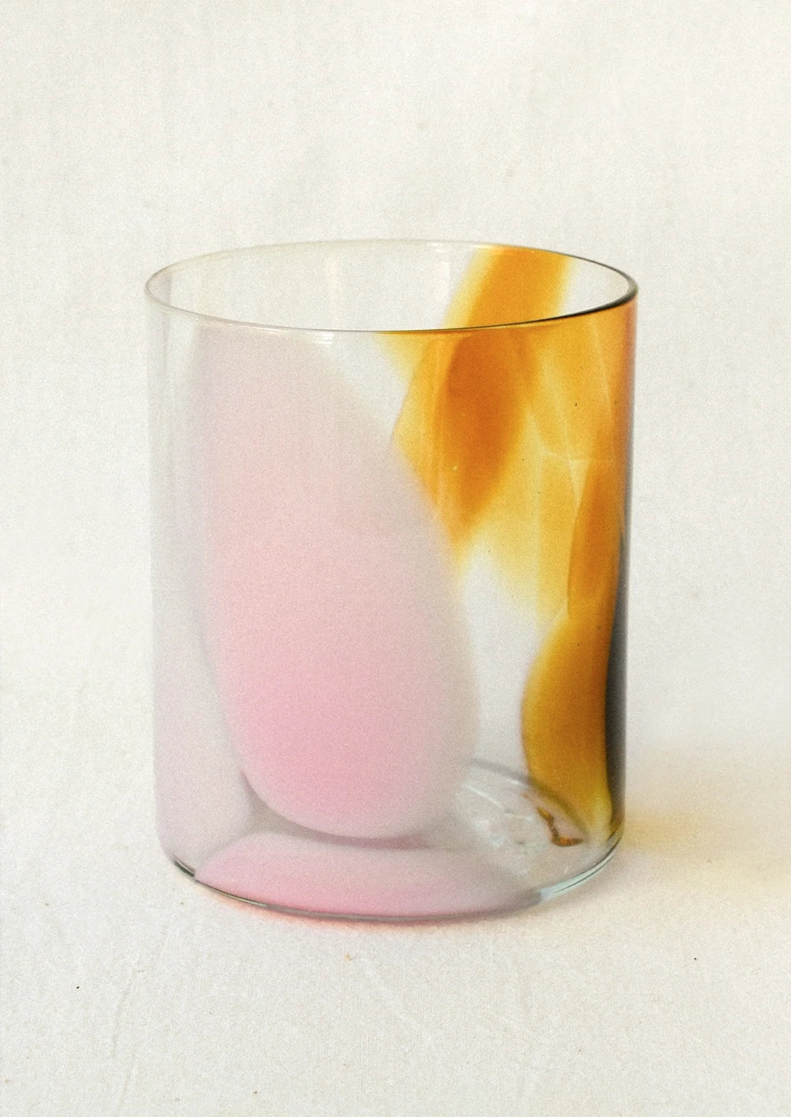 A clear glass tumbler with an abstract brown and pink design.