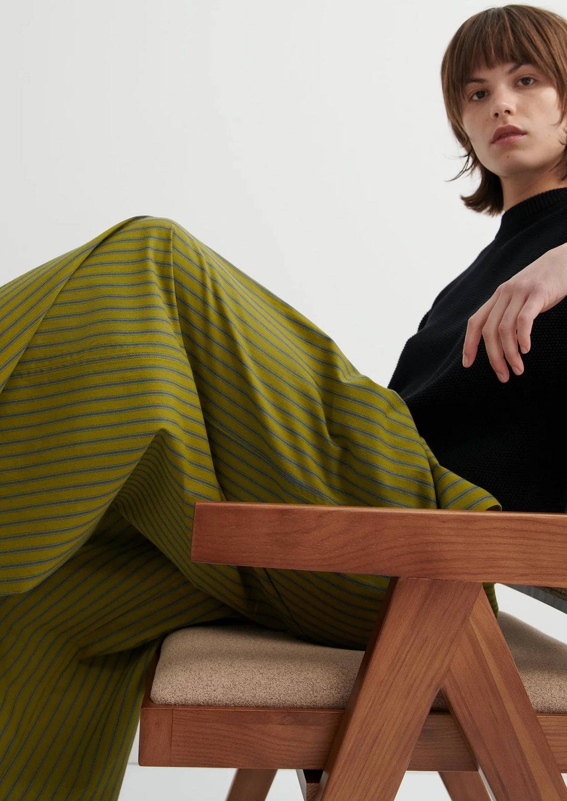 Person sitting on a wooden chair with a green striped fabric draped over them against a white background
