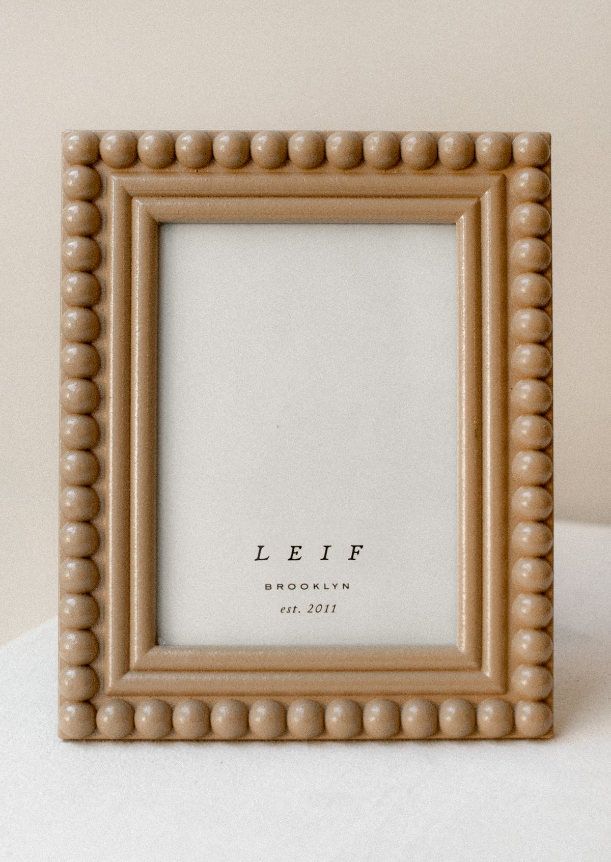 A picture frame with hobnail border in camel colored lacquer.