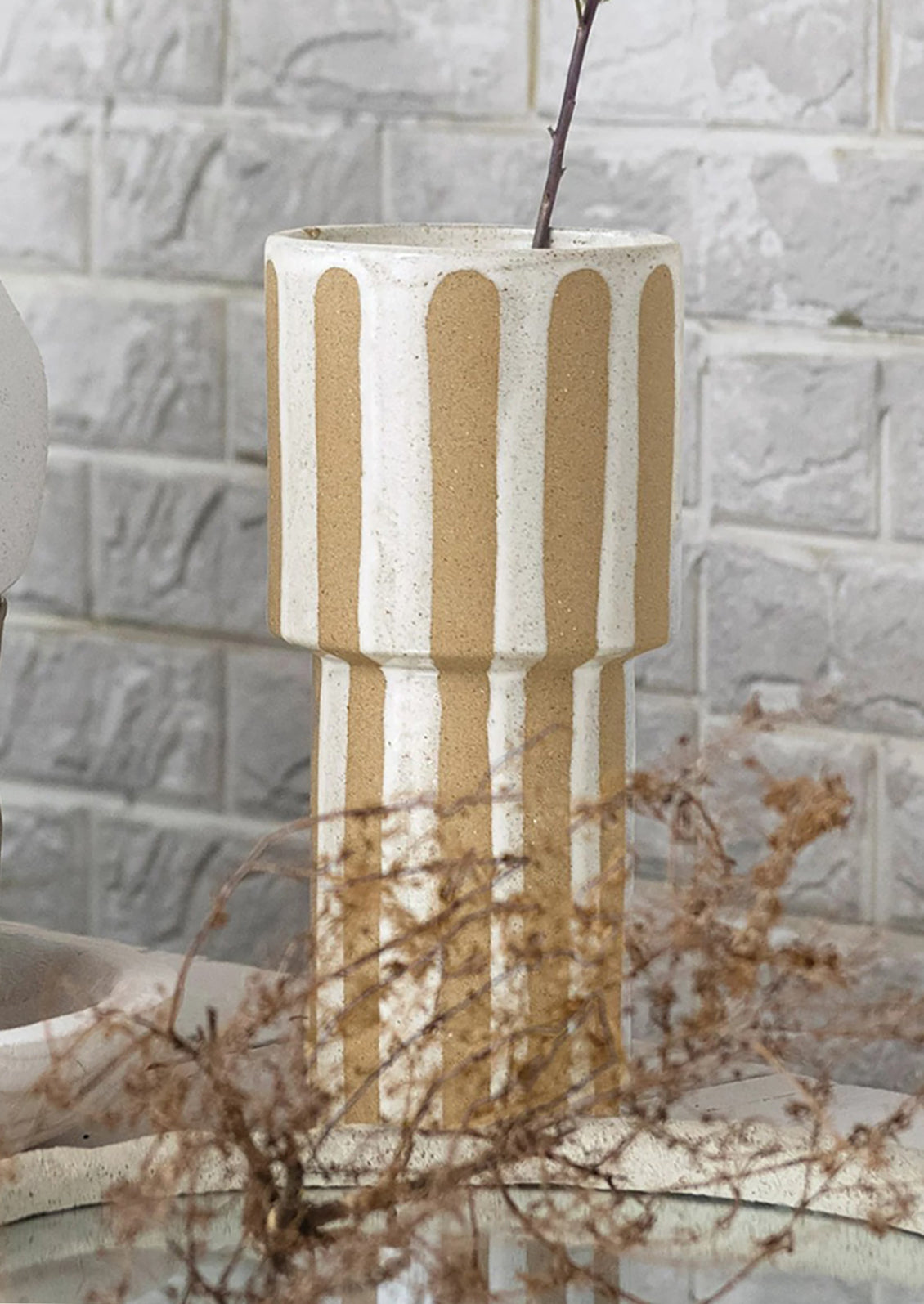 A tall sculptural vase with sandy and white vertical stripes.