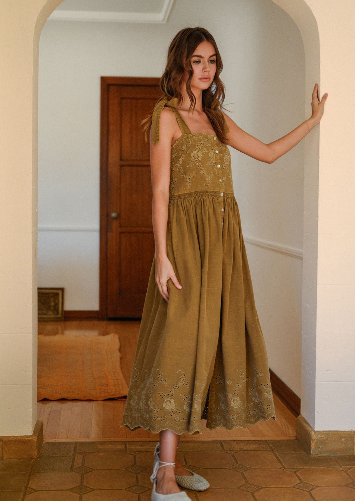 A woman wearing a greenish-brown sleeveless tie shoulder dress with tonal floral eyelet embroidery.