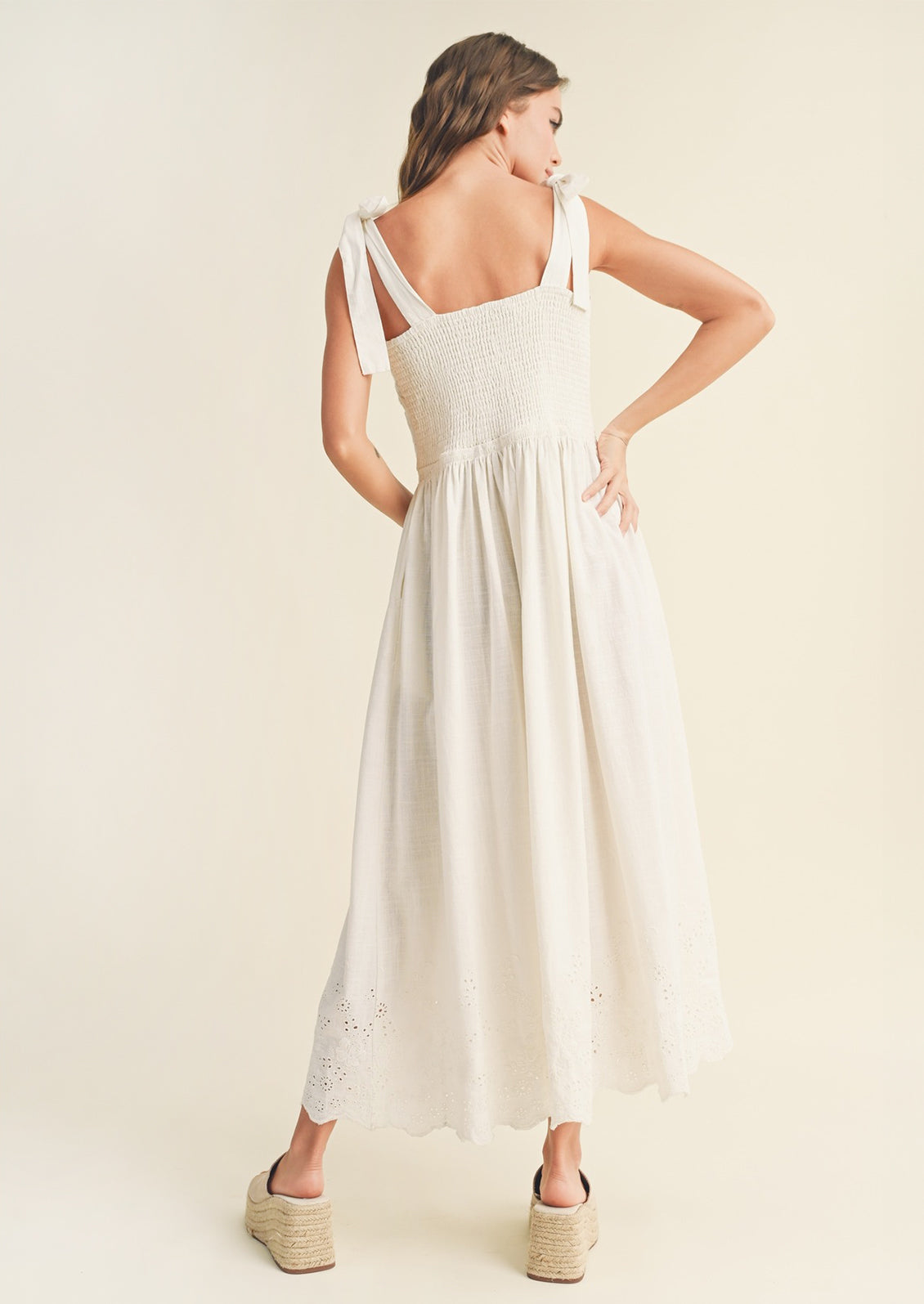 A woman wearing a white sleeveless tie shoulder dress with tonal floral eyelet embroidery.