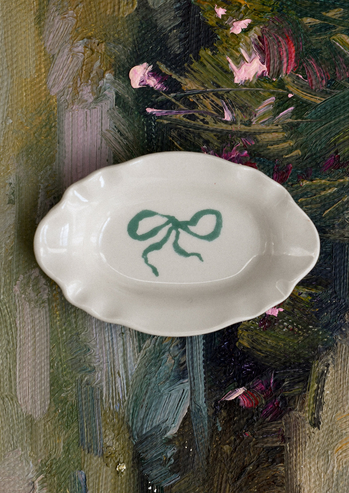 A small porcelain dish with ornate shape and hand painted bow illustration in green.