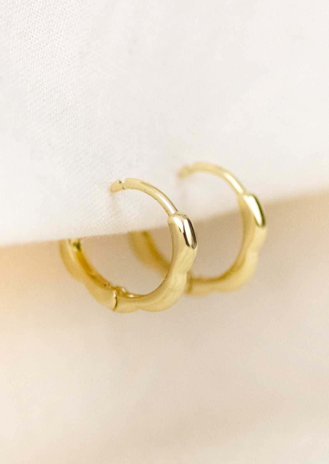 A pair of small gold hoop earrings with a scallop edge design