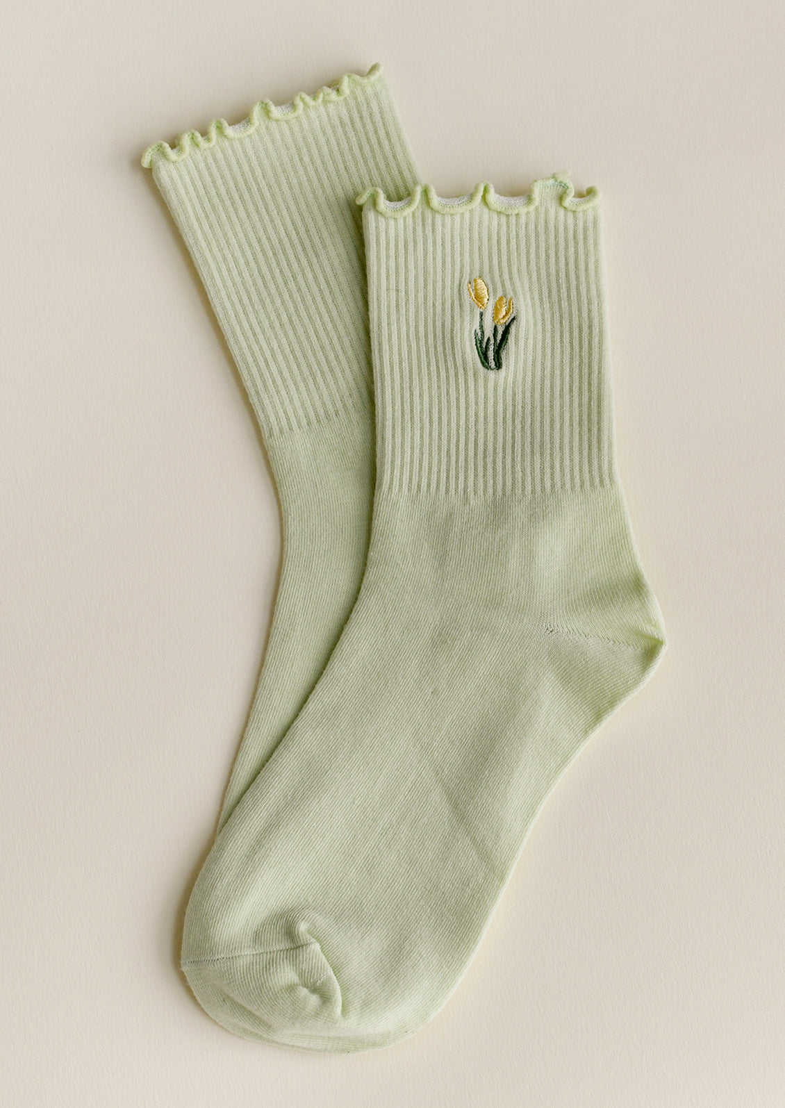 A pair of mint green socks with embroidered tulip motif in butter yellow.