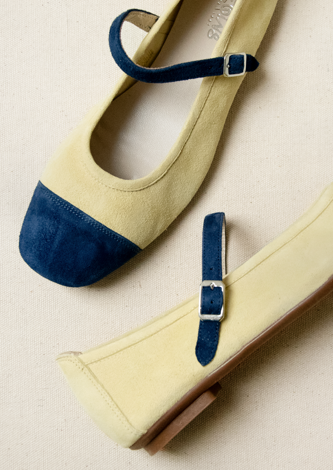 A pair of ballet flats in butter yellow with navy contrast.