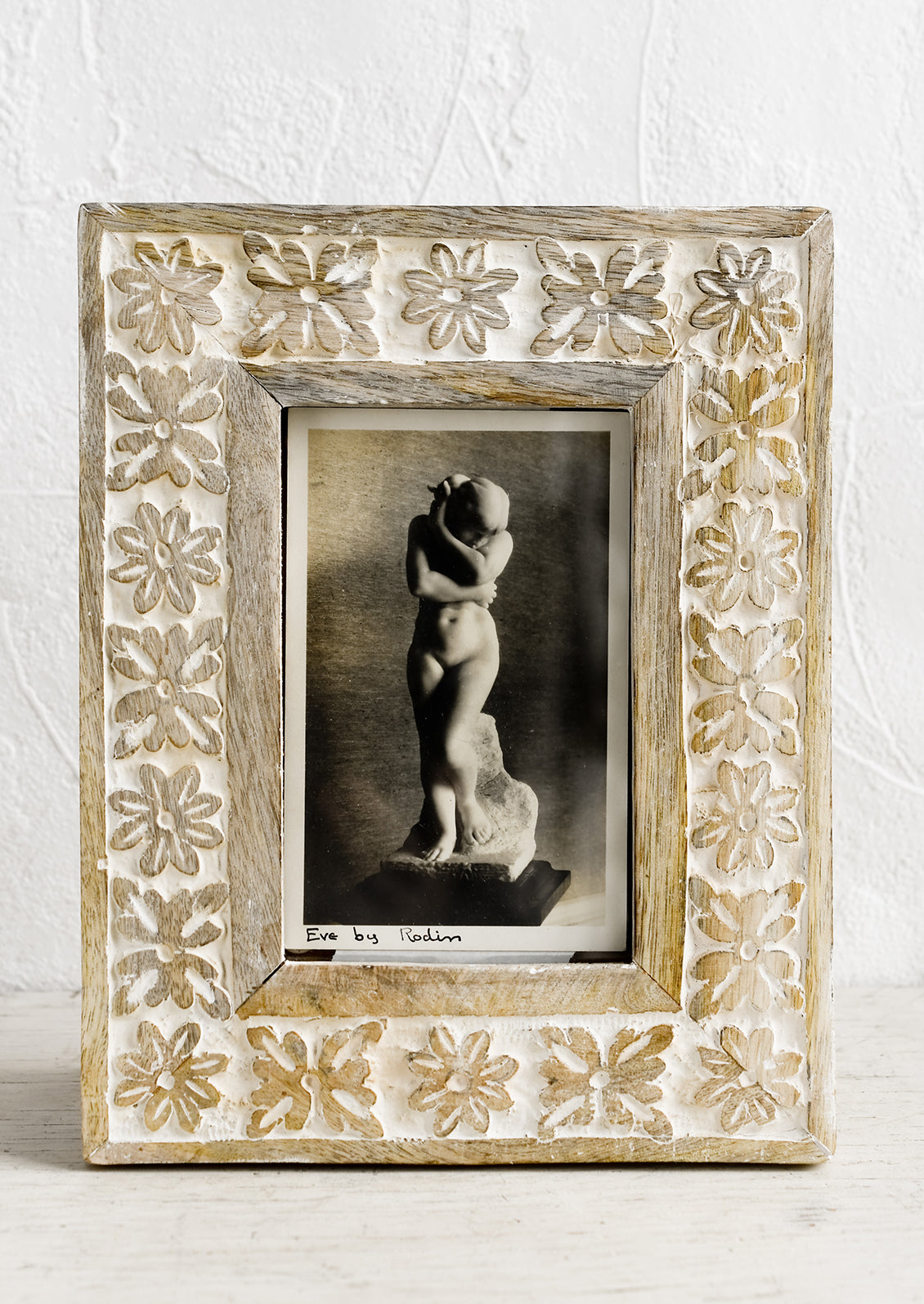 A wooden picture frame with carved whitewash floral design.