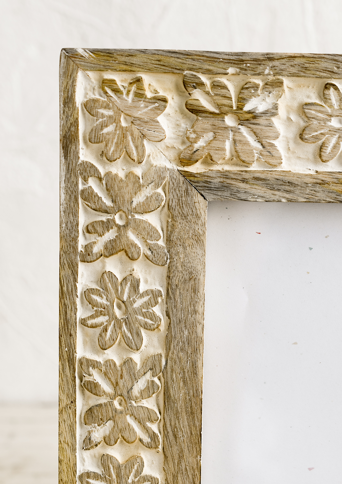 A wooden picture frame with carved whitewash floral design.