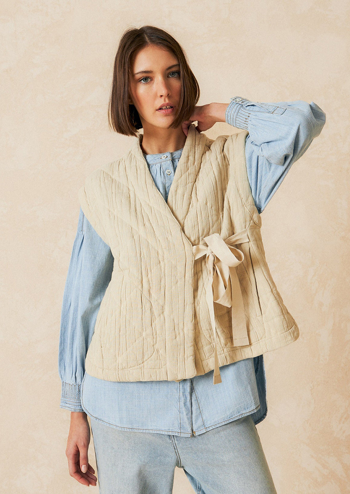 A tie front vest in cream with quilted texture and sash tie front.