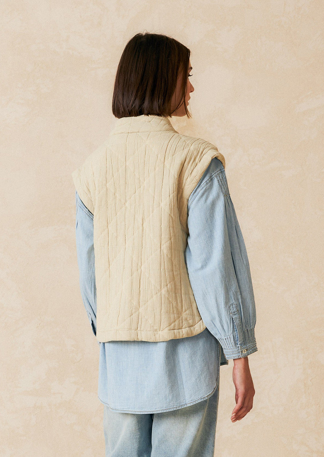 A tie front vest in cream with quilted texture and sash tie front.