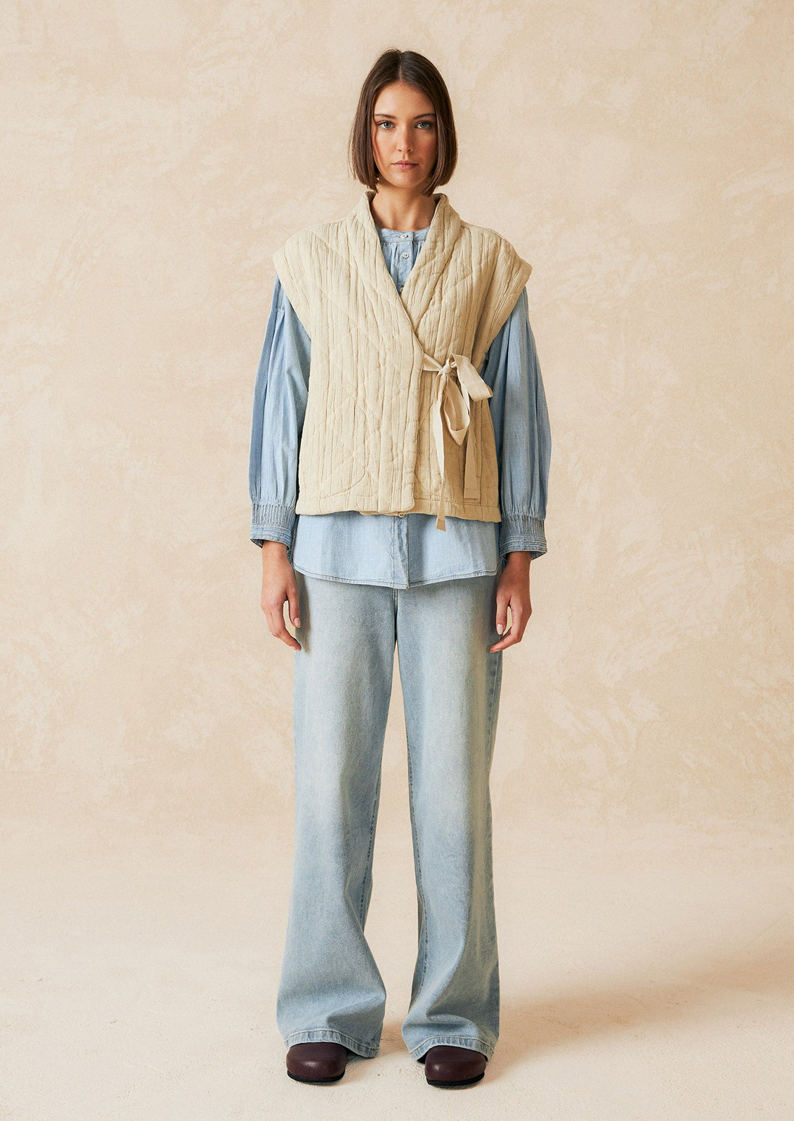 A tie front vest in cream with quilted texture and sash tie front.