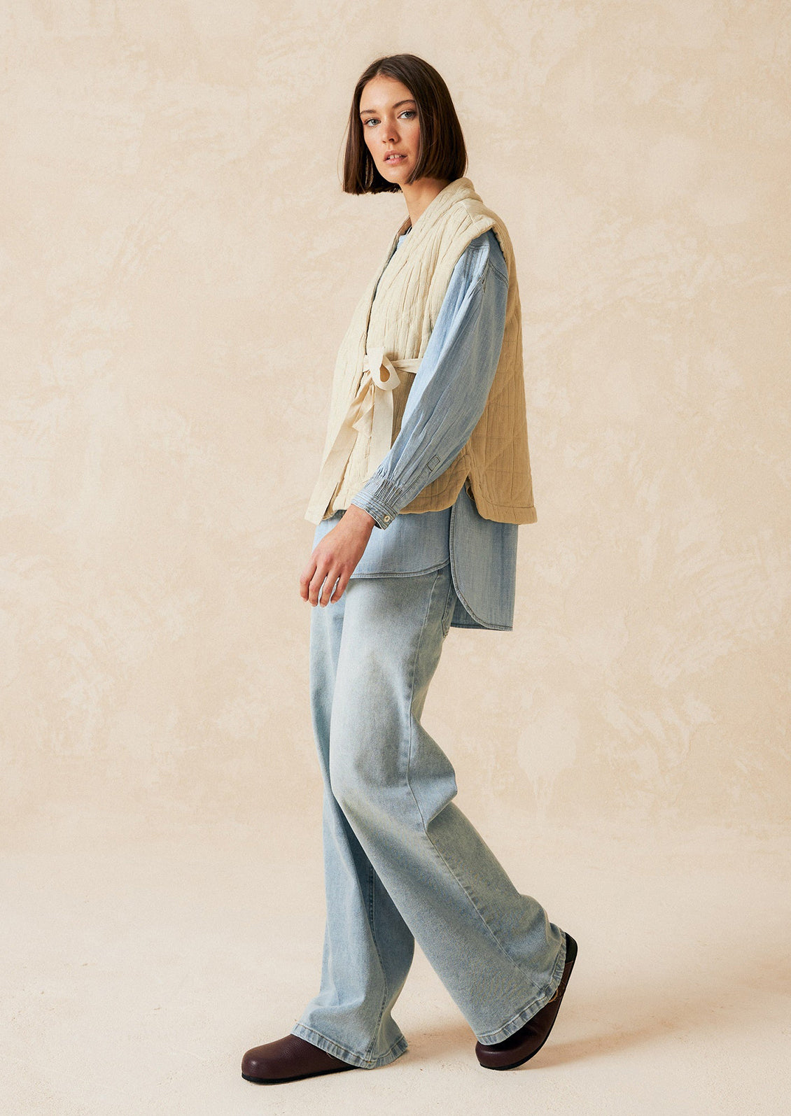 A tie front vest in cream with quilted texture and sash tie front.
