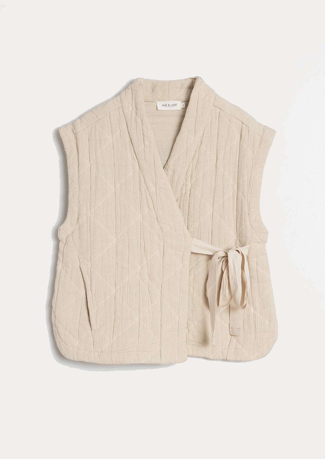A tie front vest in cream with quilted texture and sash tie front.