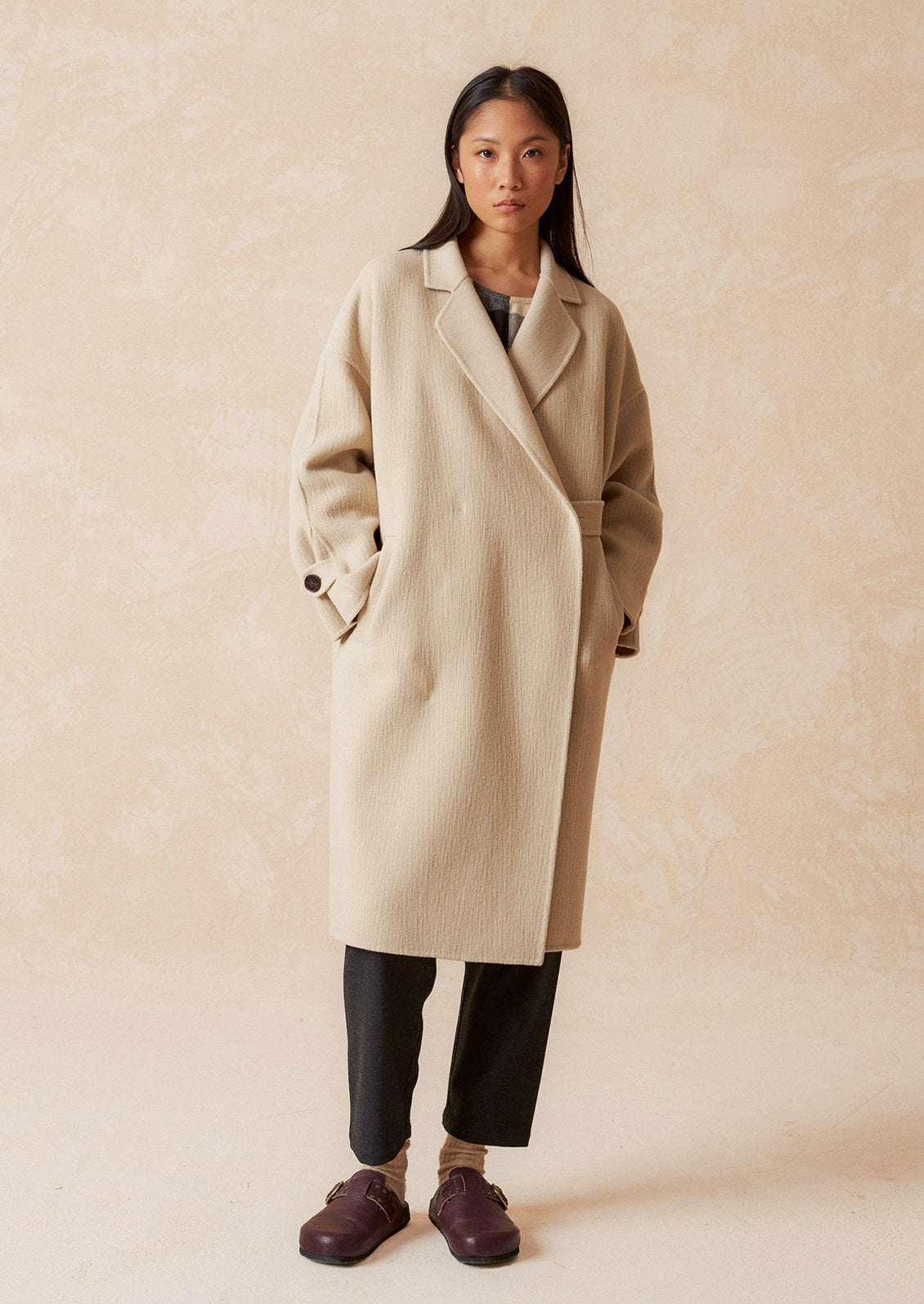 A woman wearing a wool coat with subtle texture and tab closure.