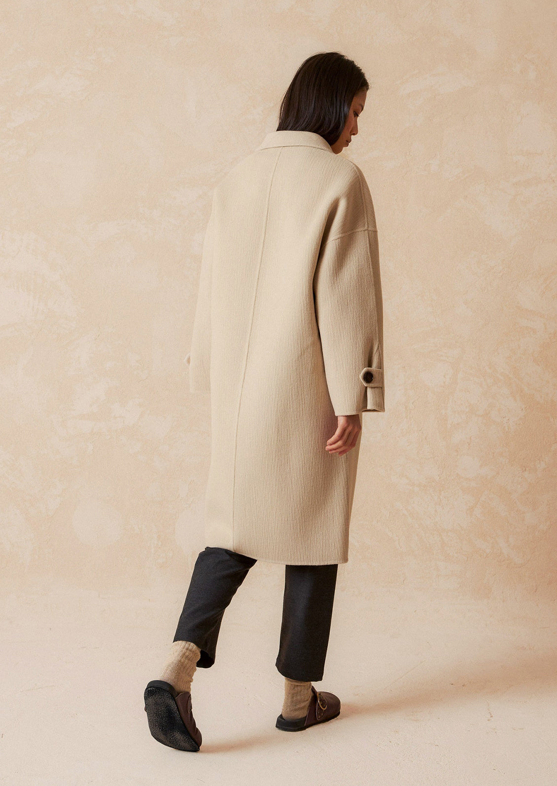 A woman wearing a wool coat with subtle texture and tab closure.
