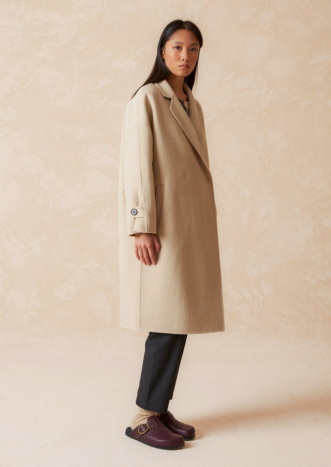 A woman wearing a wool coat with subtle texture and tab closure.