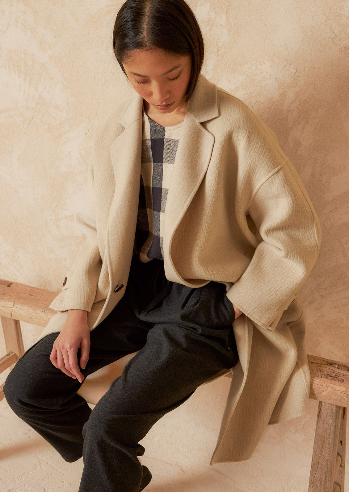 A woman wearing a wool coat with subtle texture and tab closure.
