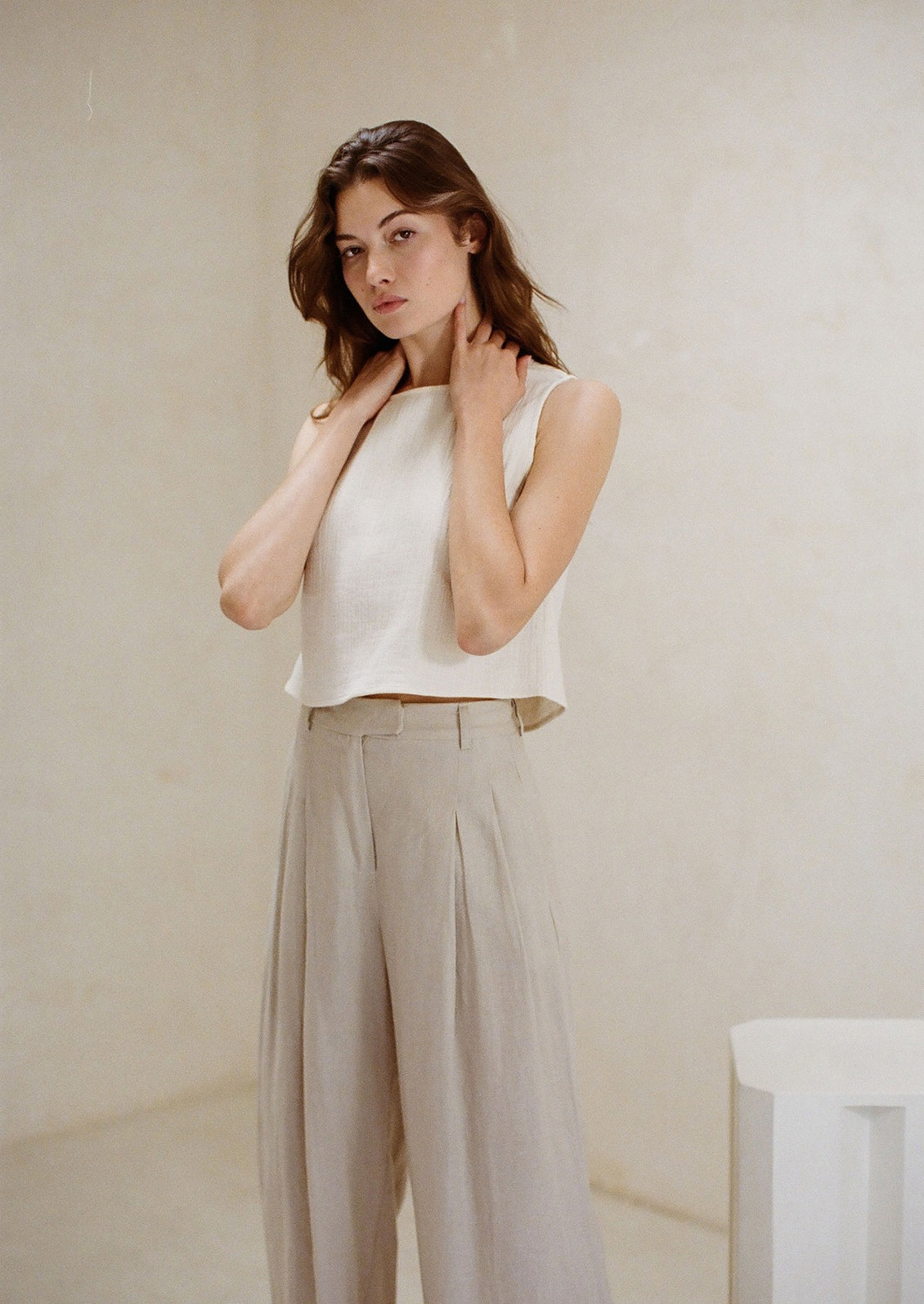 A woman standing wearing a white cotton gauze tank top and neutral long pants