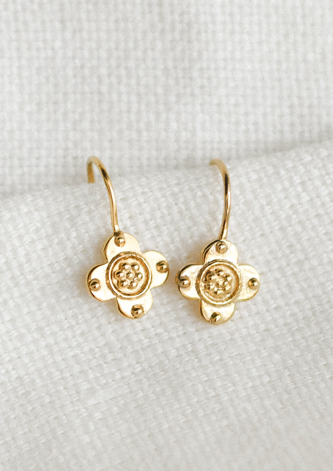 A pair of clover shaped gold earrings with raised bead texture.