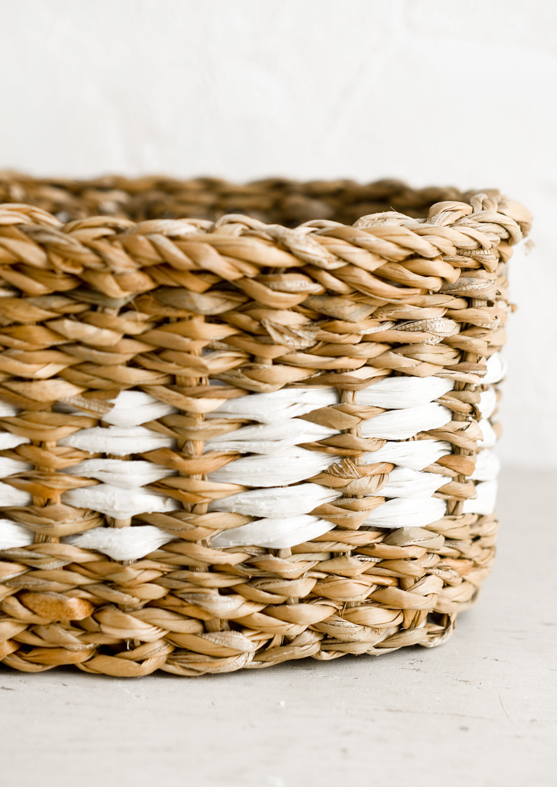 An oval shaped storage basket in seagrass with woven white detail.