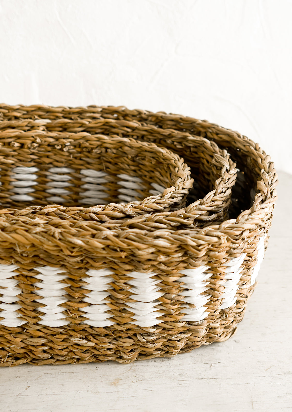 An oval shaped storage basket in seagrass with woven white detail.