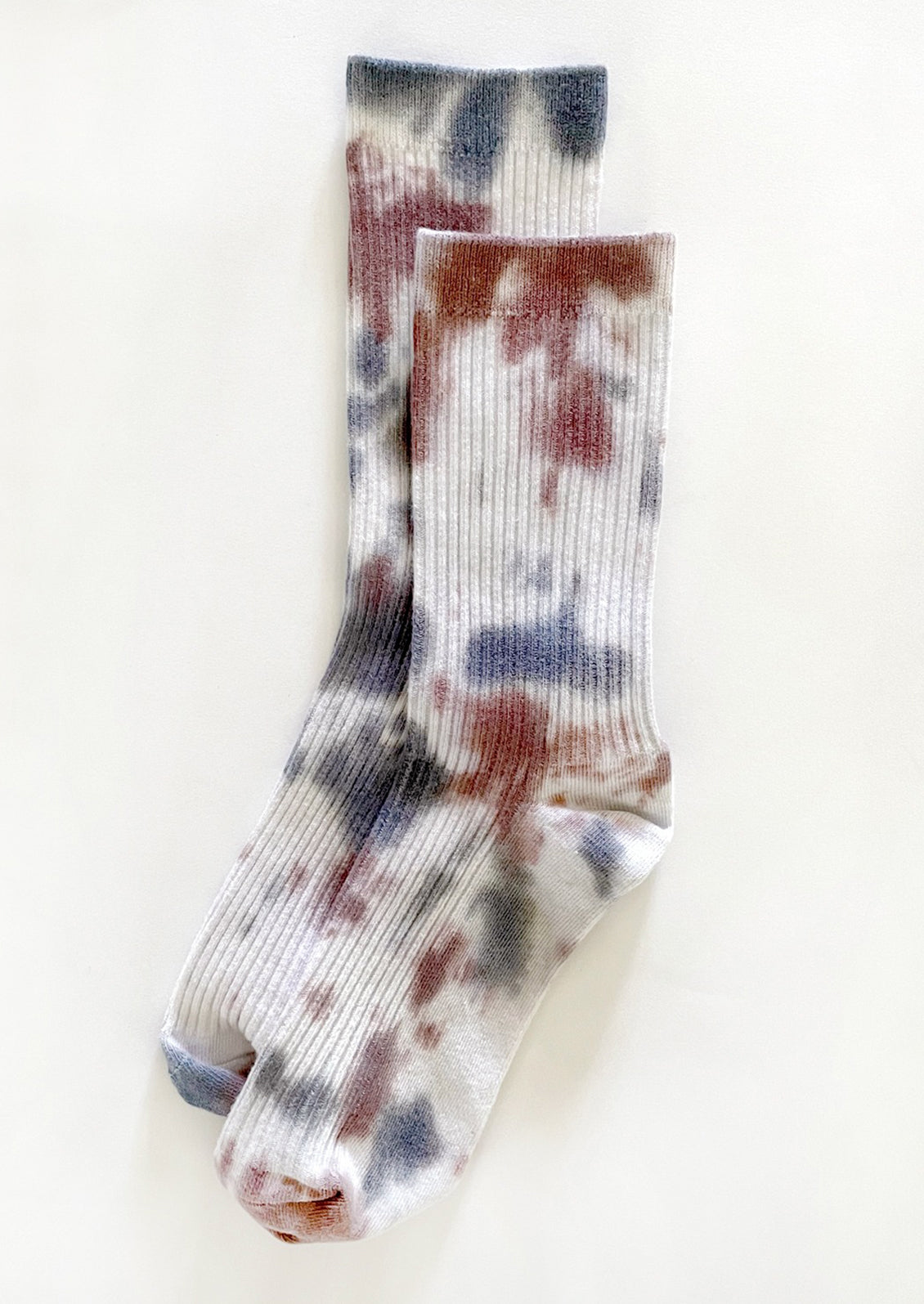 A pair of tie dye socks in white with maroon and blue.