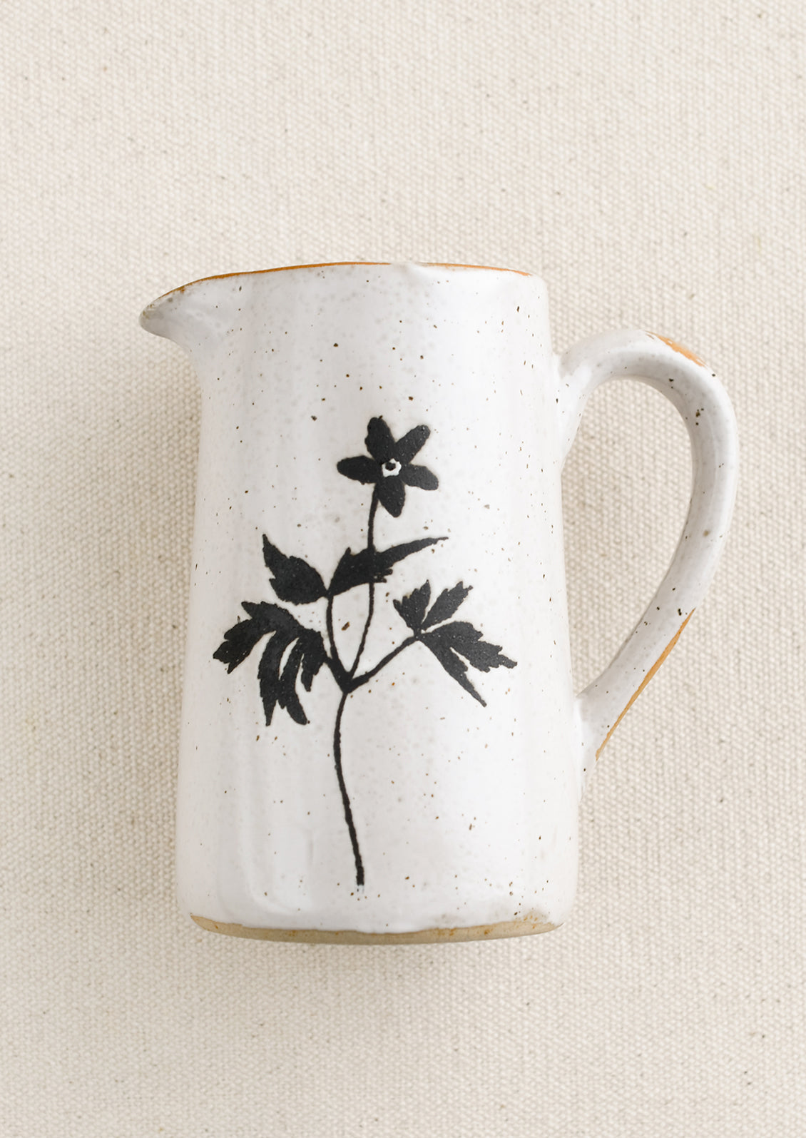 A small speckled white ceramic creamer pitcher with black flower silhouette.