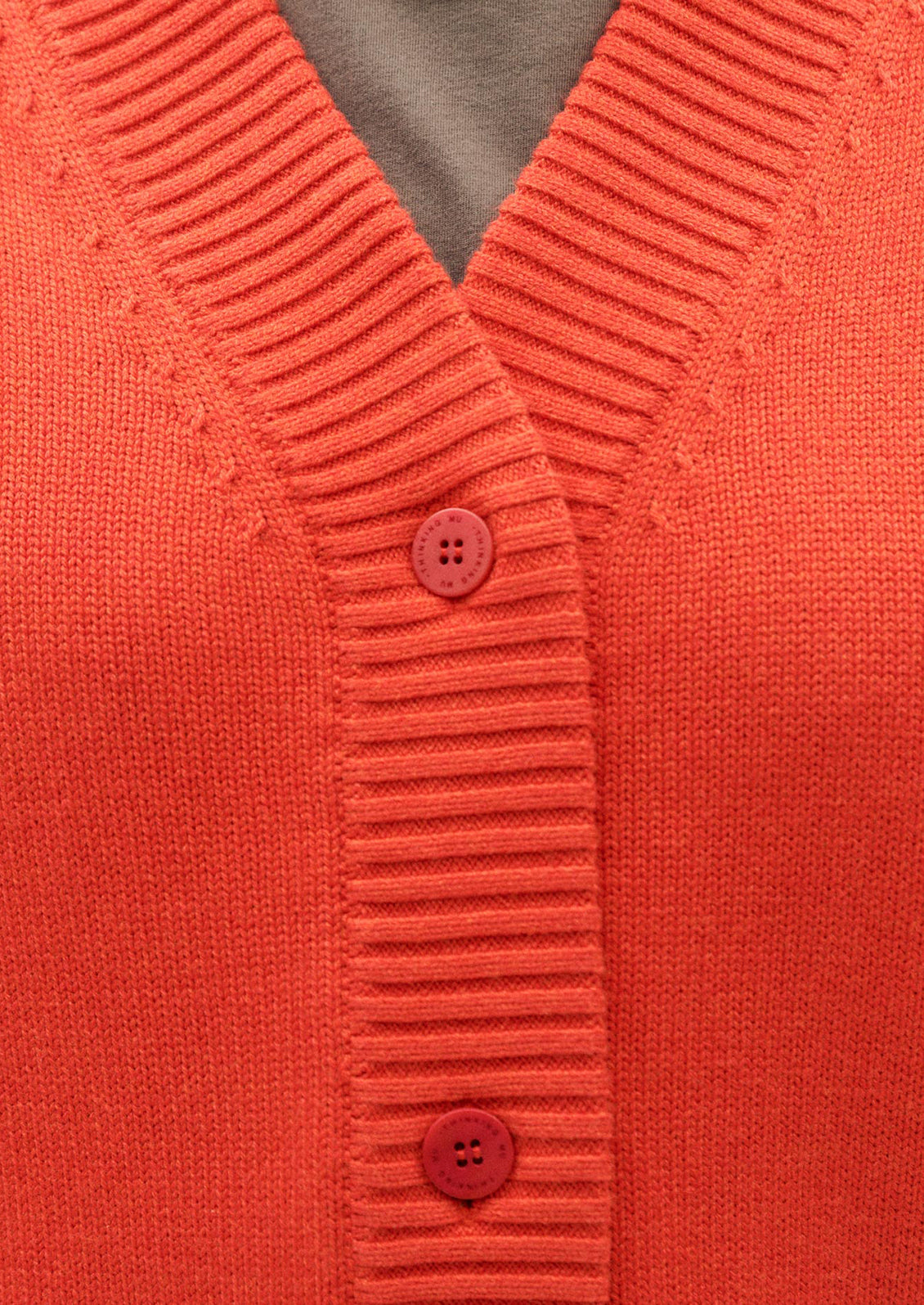A woman wearing a button front, long sleeve cardigan sweater in red-orange huge.