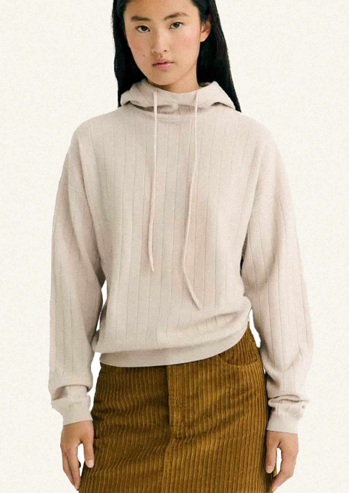 Woman wearing a beige ribbed hoodie and brown corduroy skirt on a white background