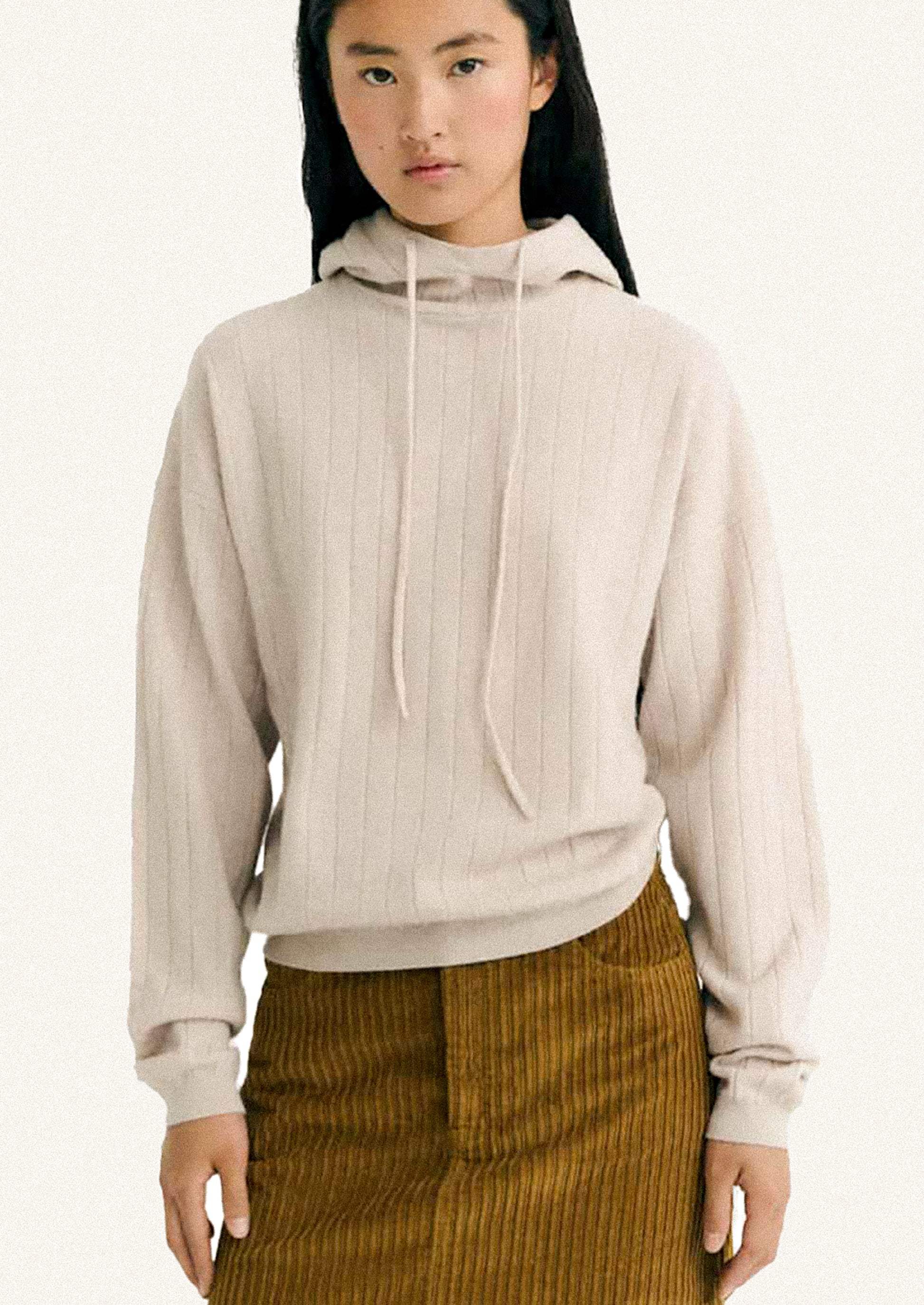 Woman wearing a beige ribbed hoodie and brown corduroy skirt on a white background