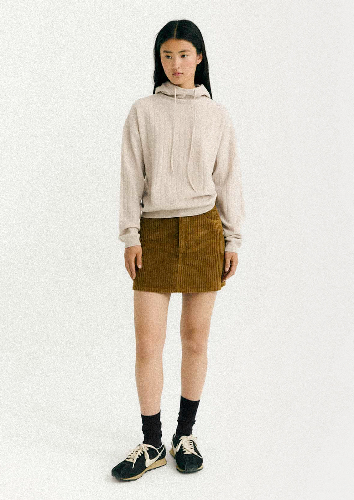 Person wearing a beige hoodie and brown skirt on a white background