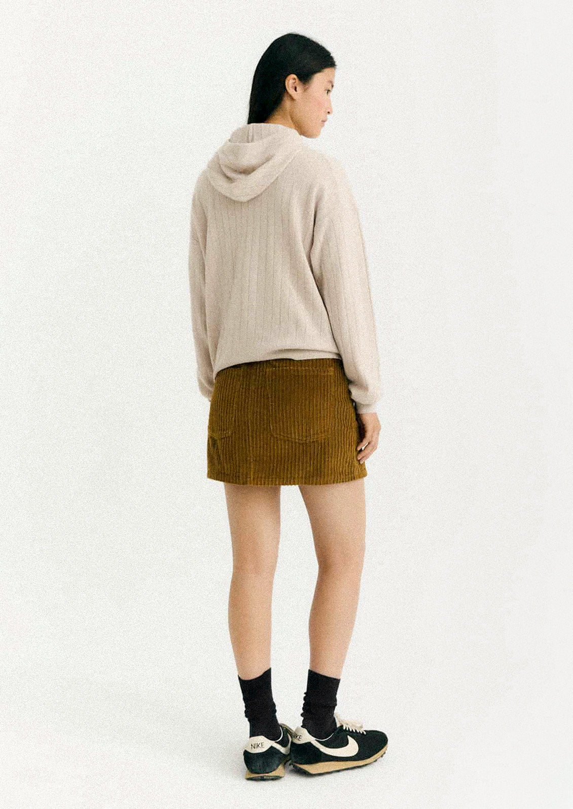 Person wearing a beige hoodie and brown skirt on a white background
