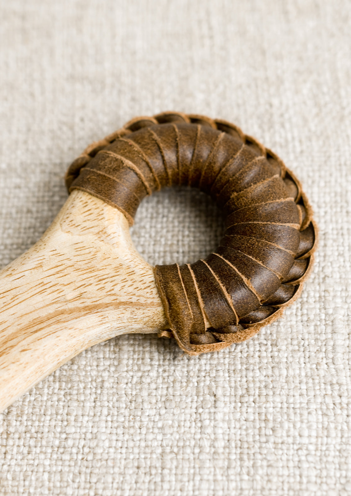 A paddle shaped light wood cutting board with brown leather wrapped handle.