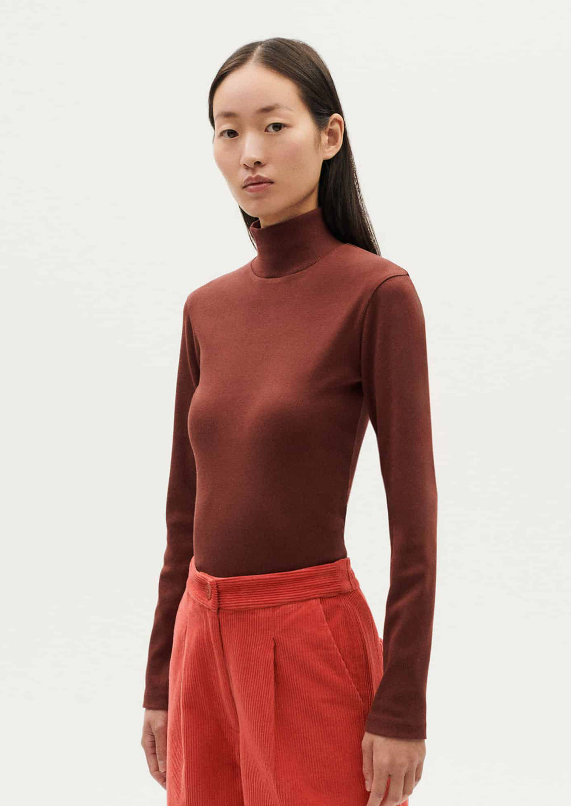 A woman wearing a form fitting, long sleeve turtleneck t-shirt in brown.