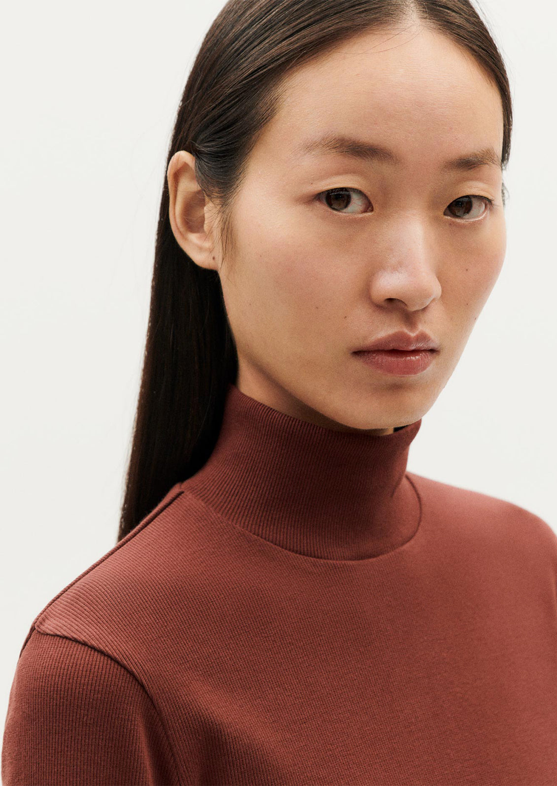 A woman wearing a form fitting, long sleeve turtleneck t-shirt in brown.