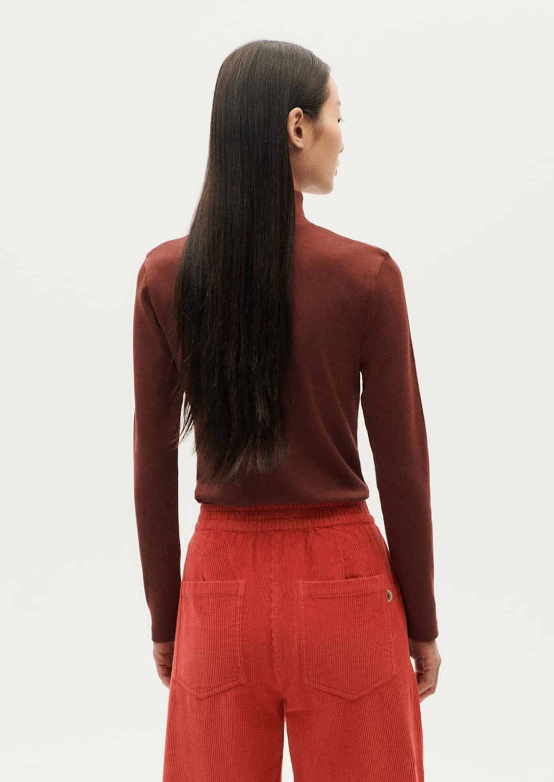 A woman wearing a form fitting, long sleeve turtleneck t-shirt in brown.