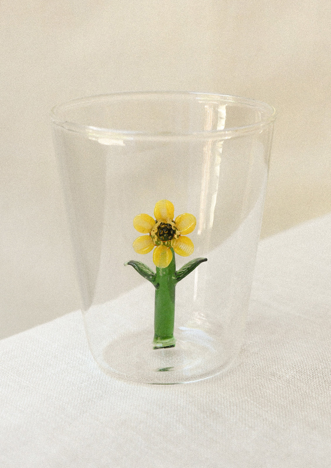 Clear drinking glass with a yellow sunflower charm inside glass.