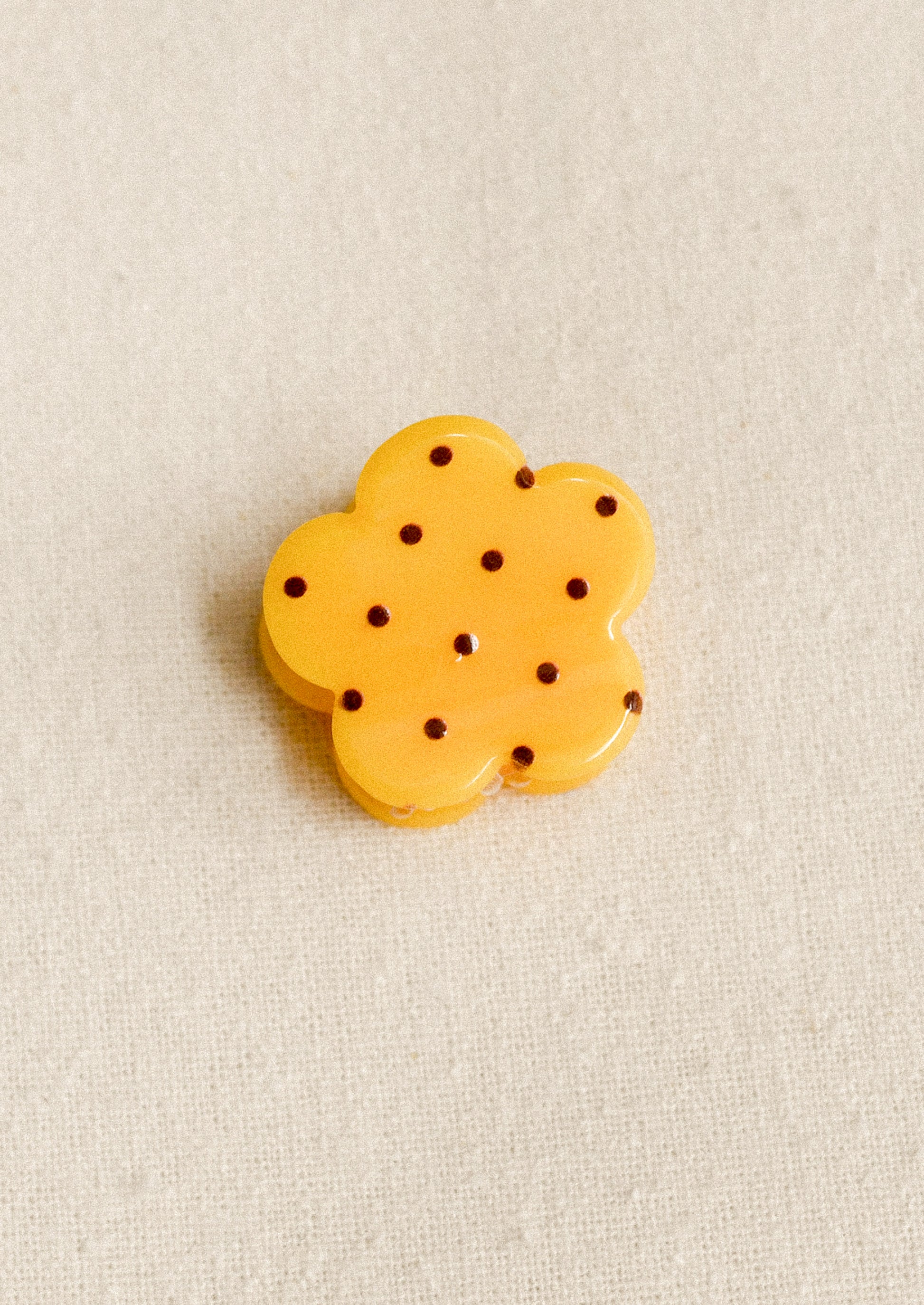 A small flower shaped hair clip in yellow with burgundy polka dots.