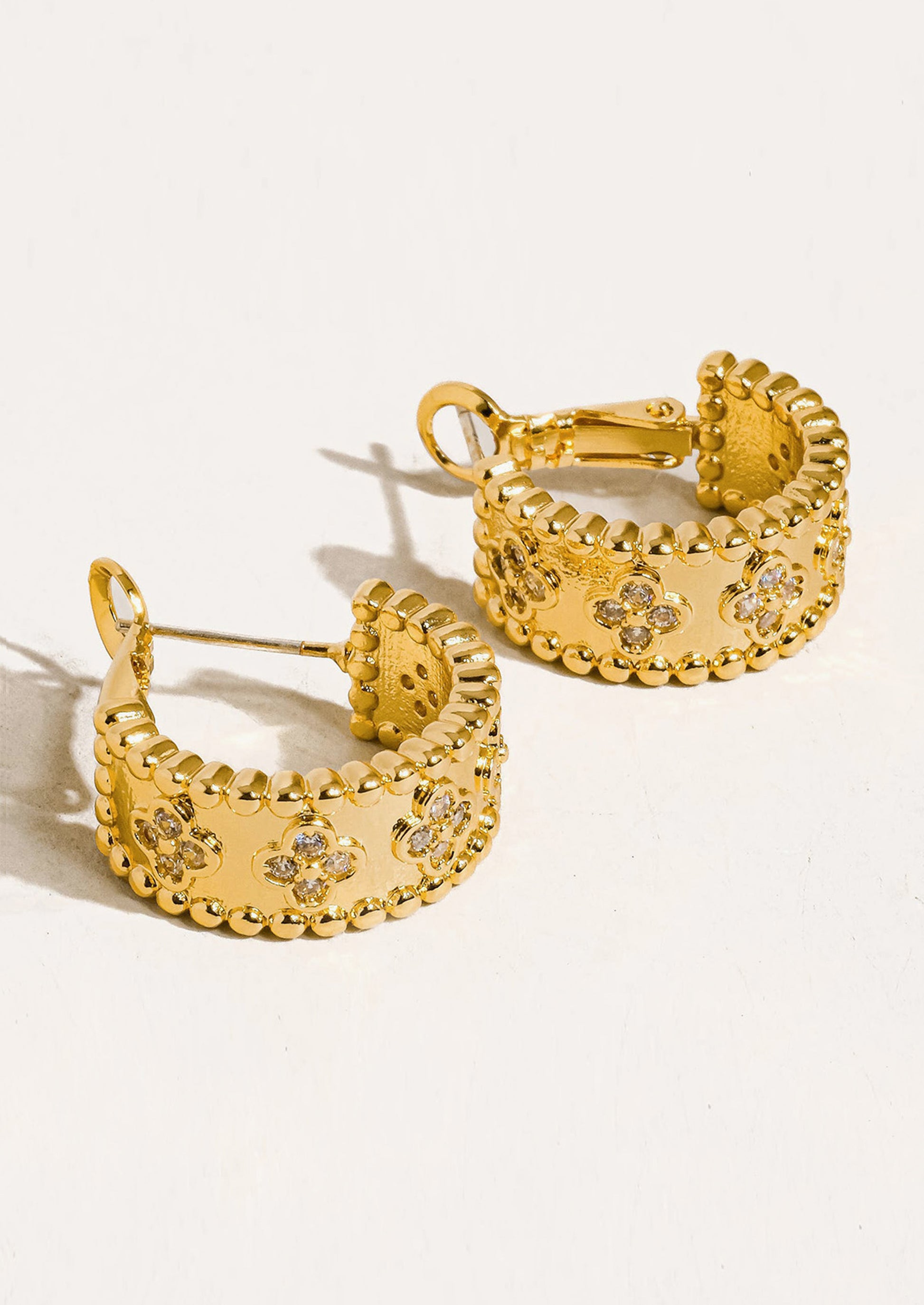 A pair of ornate thick gold hoop earrings.