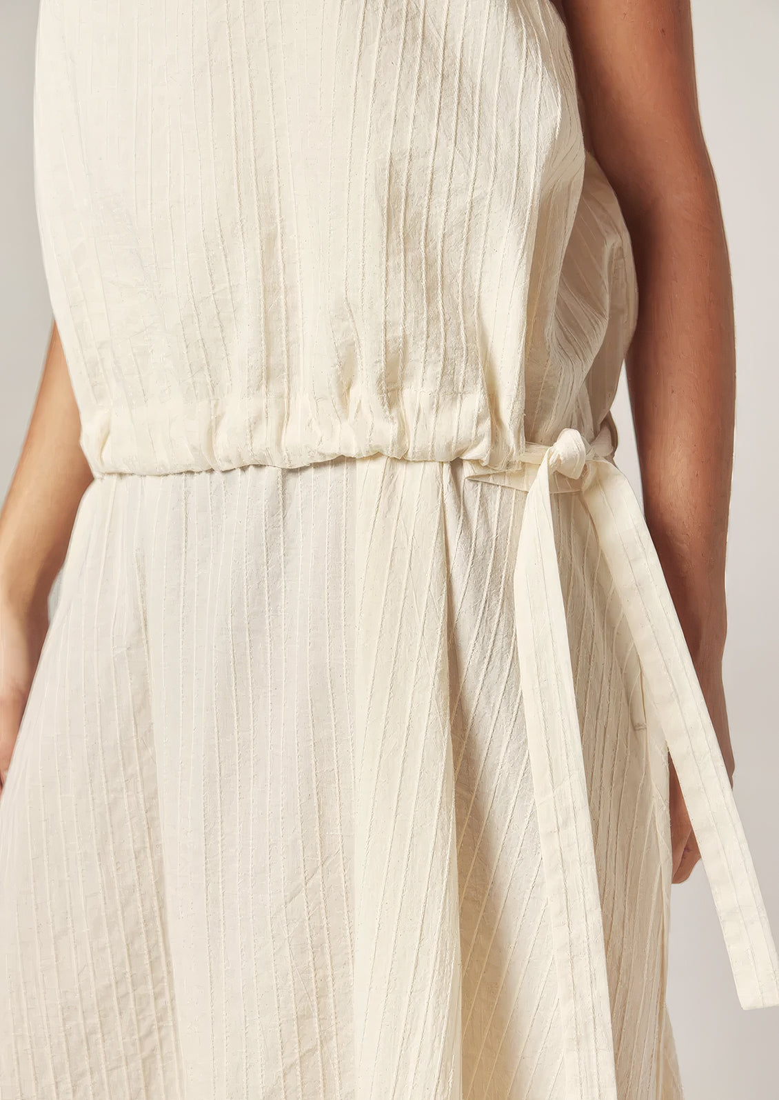 A person wearing a cream cotton dress with tonal stripe pattern.