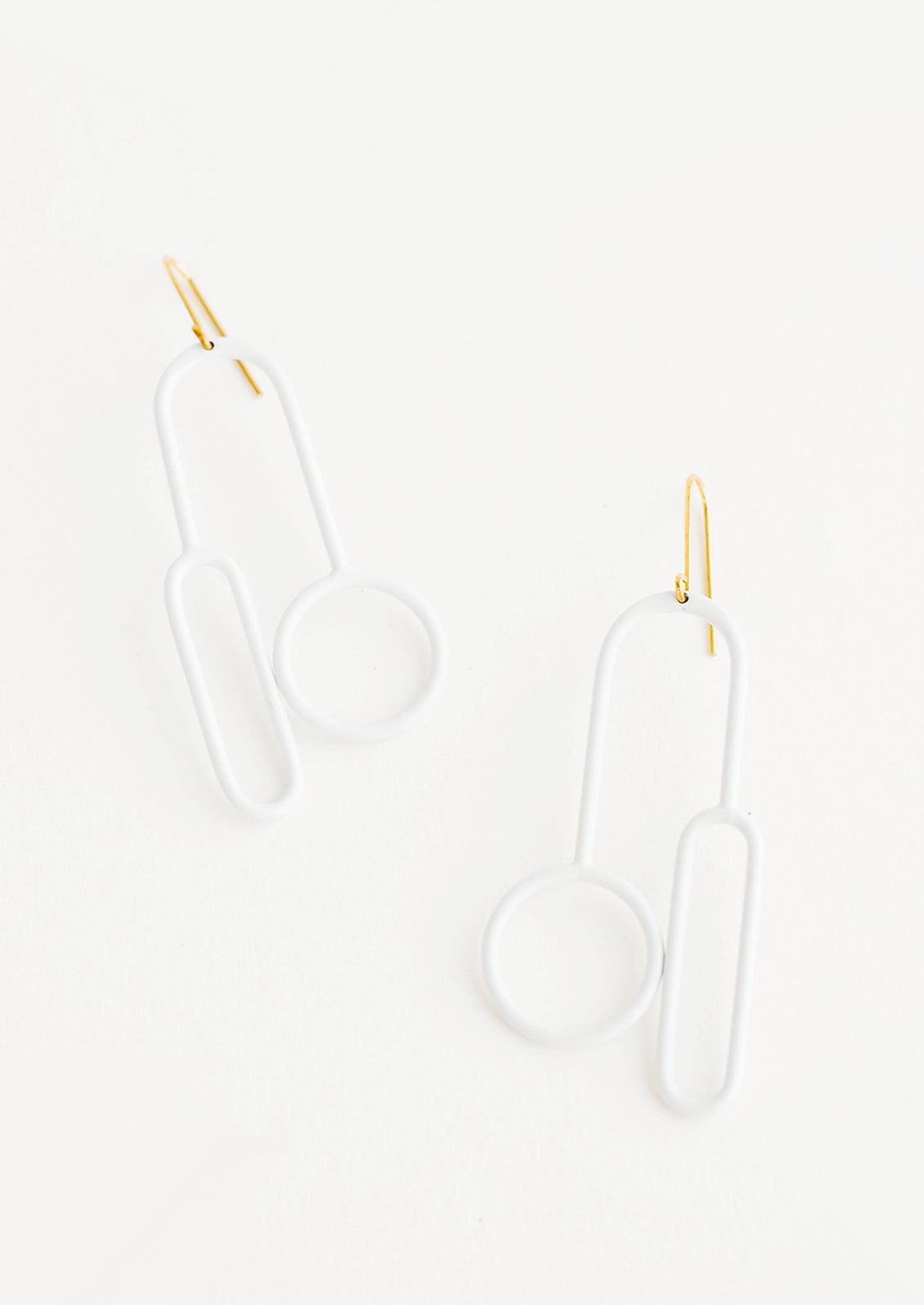 Arced white earrings with one circle and one elongated oval at either end on a brass ear wire. 