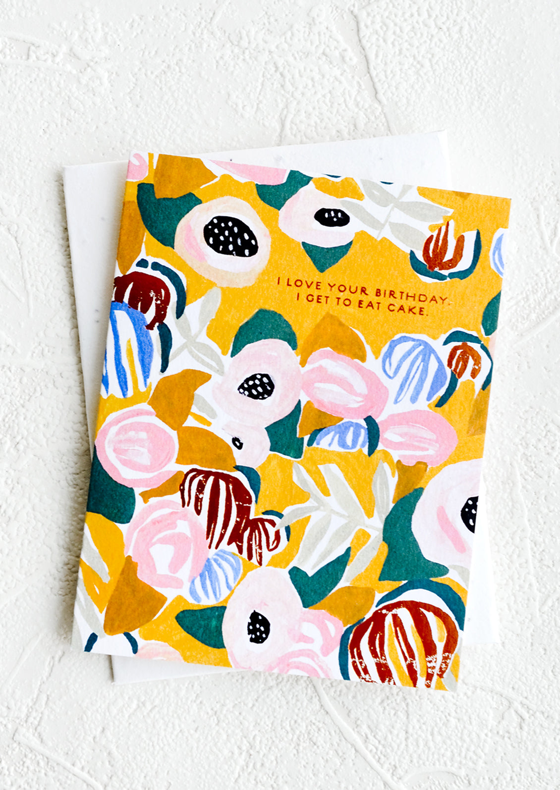 A floral patterned greeting card with yellow background and copper text reading "I love your birthday I get to eat cake".