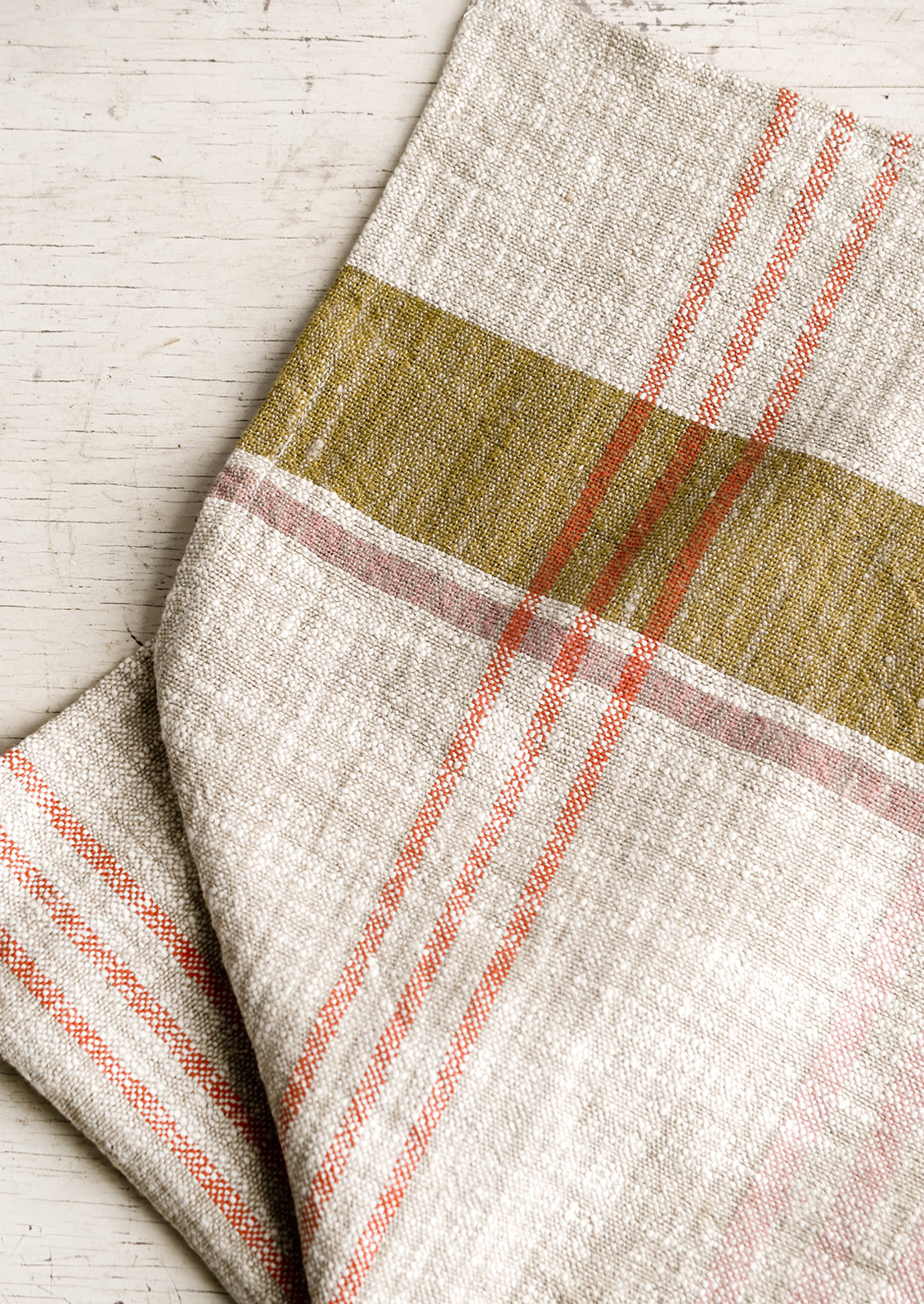 A natural tea towel with orange, ochre and pink plaid pattern.