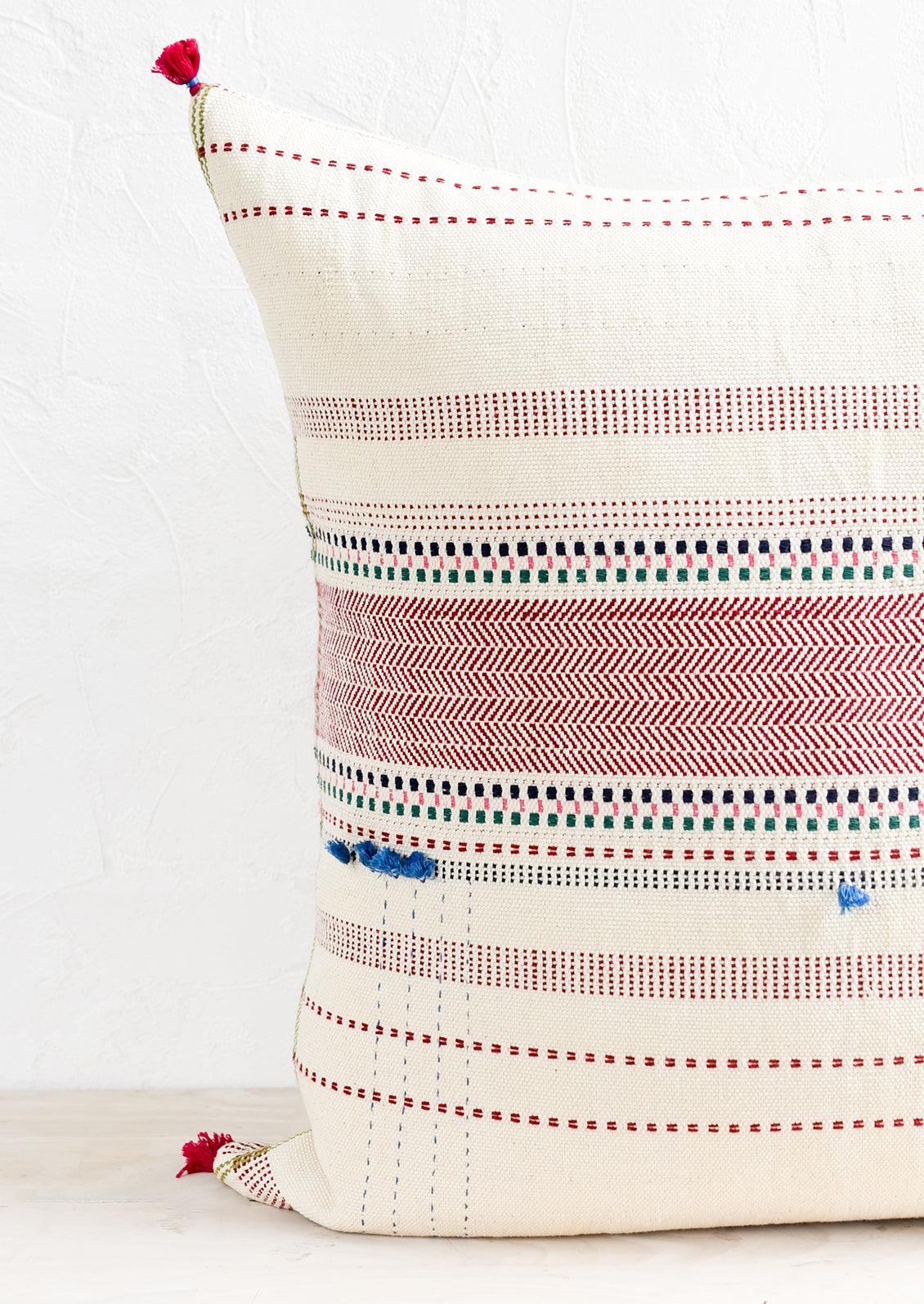 A cotton throw pillow with multicolor and red embroidery and tassel detailing.